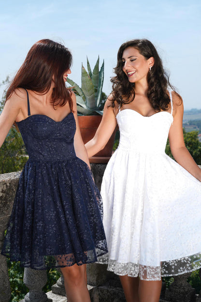 Due abiti midi eleganti in tlle ricamato, uno bianco e uno blu notte, indossati all’aperto per cerimonia